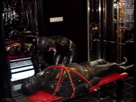 Mask - The slave is tied with leather straps to a wallcross. The mistress now has full control over tha slave. She controls his cock, his rubber dressed body and his breathing. No control for the slave, he will surrender to the mistress.